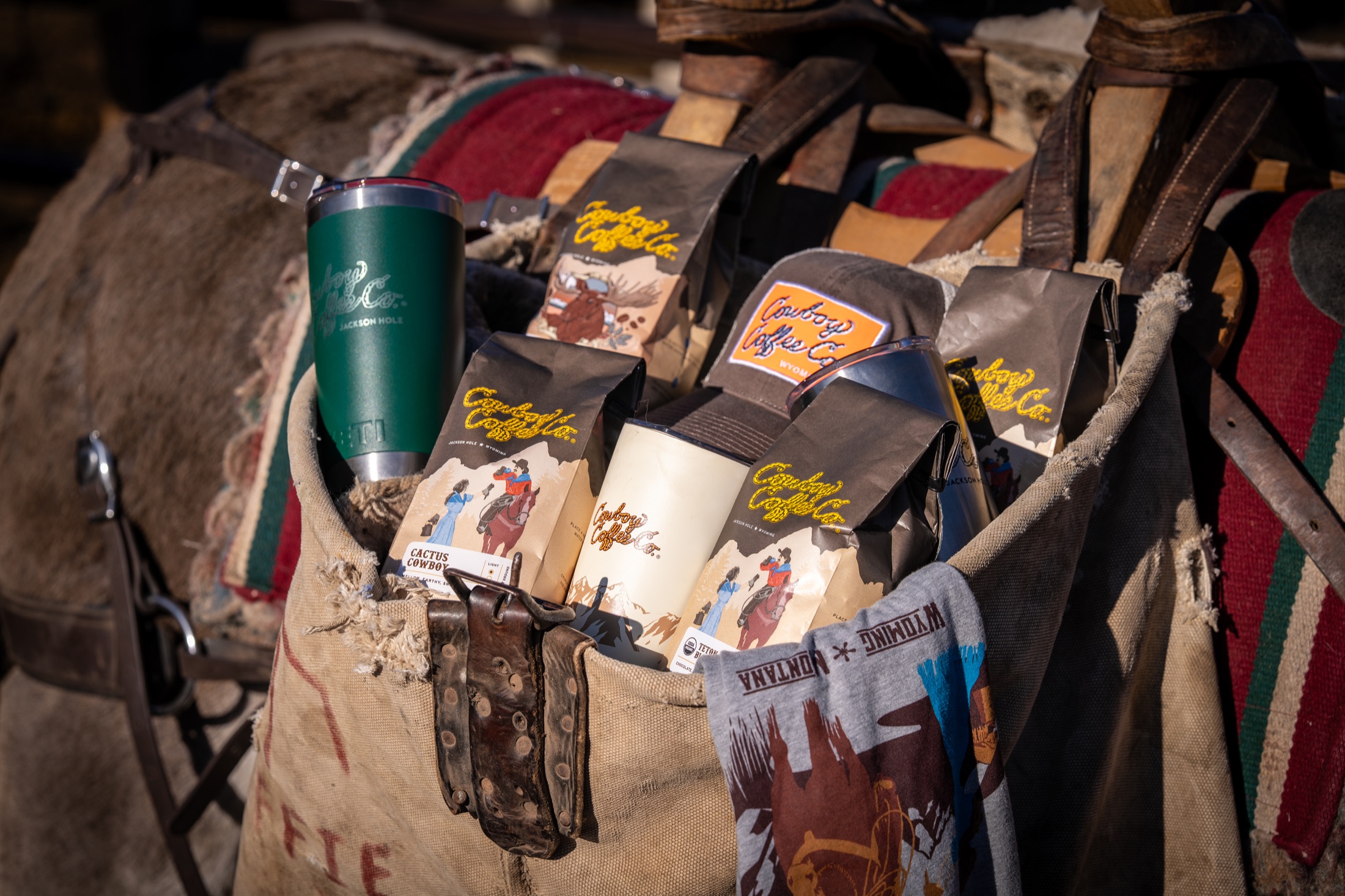 Cowboy Coffee bags, tumblers, hats, and a Wyoming bandana packed in canvas saddlebags